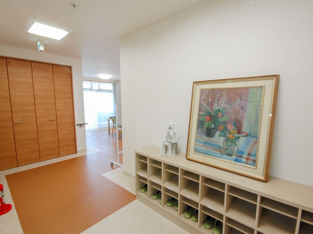 大きな収納スペースが付いた玄関には白いオープンタイプの靴箱も置かれ、大きな絵画が飾られている。