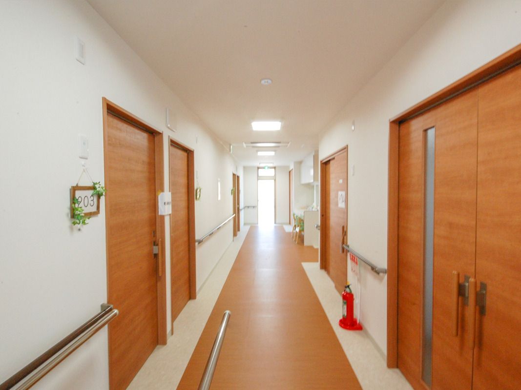 両サイドに居室のドアや手すりが設置されたまっすぐな廊下。手前にある居室のドアにはフェイクグリーンが飾られている。