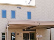 2階建ての建物はベージュ系でまとめられ、玄関先には車寄せがあり、ホーム名が書かれたプレートが貼られている。