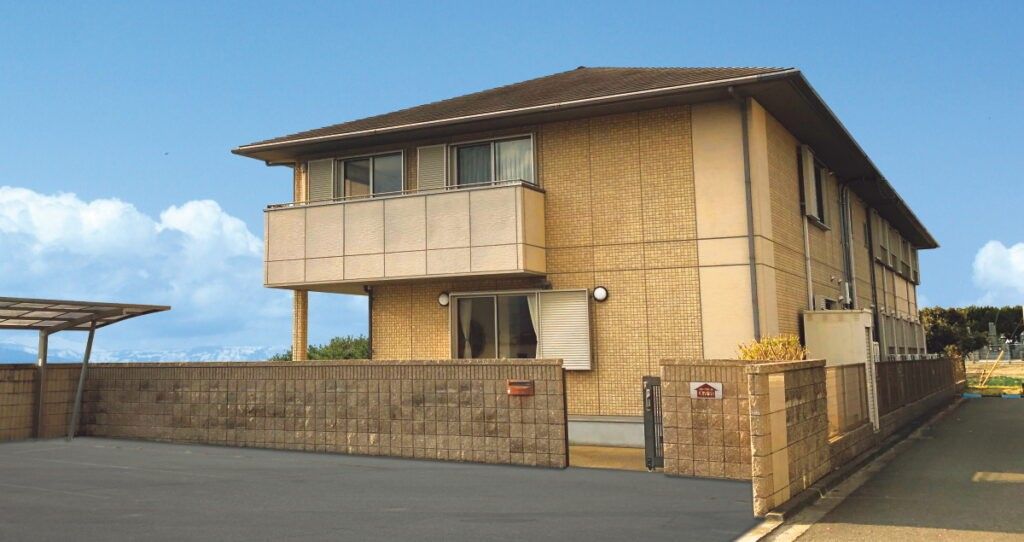 原っぱのような場所を散歩しているエプロンを付けた女性スタッフと高齢女性。顔を見合わせてほほえんでいる。