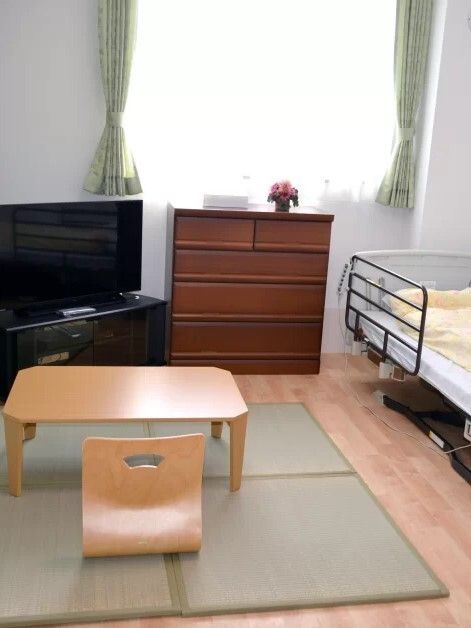 畳が敷かれたフローリングの部屋には介護ベッドやテレビ、ローテーブルなどが置かれている。