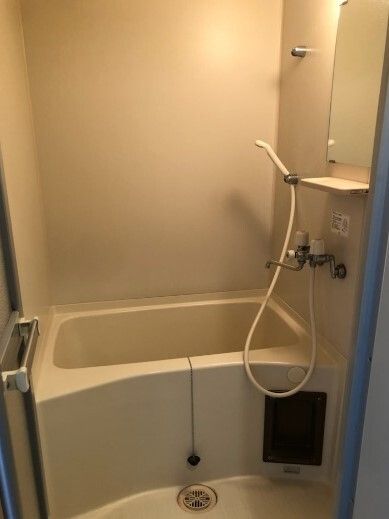 壁にシャワーや鏡が付いた一人用の浴室。深くて四角い浴槽が設置され、線をしてお湯をためるタイプ。浴槽のそばには蛇口もある。