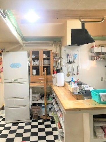 明るいキッチンは白と黒のモザイク柄のフロアで対面式のキッチンが付き、食器棚や冷蔵庫も置かれている。レンジフードの横には調理器具がかかっている。