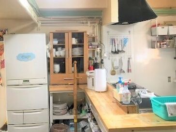 対面式のキッチンが付いた共有スペース。冷蔵庫や食器棚が置かれ、ポットや調理器具などがあり、大きなレンジフードもある。