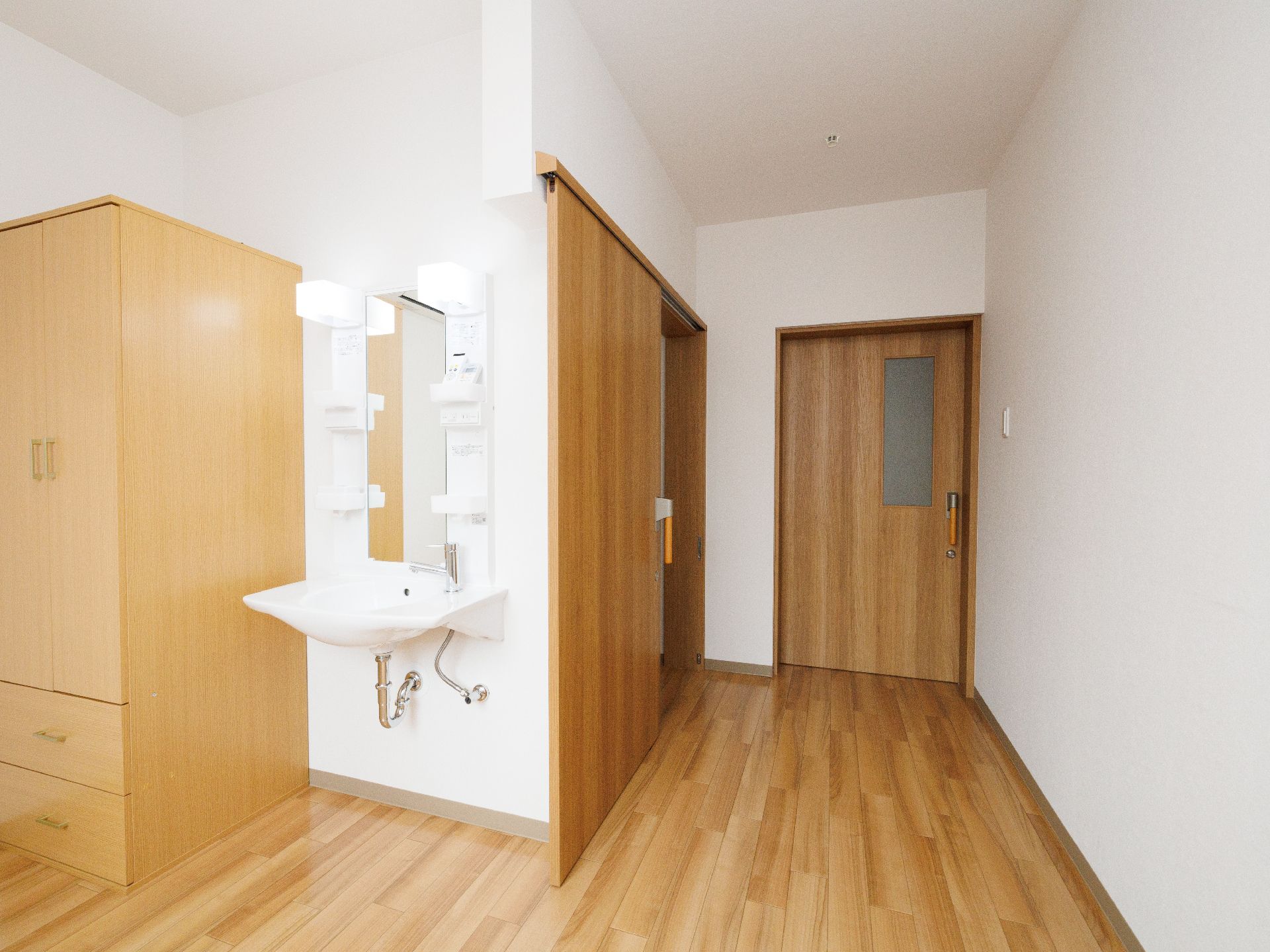 木製の棚と洗面台が配置された白い壁の部屋
