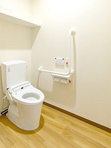 エル字型の手すりやオレンジの呼び出しボタンが付いたトイレは広く、ふたのない便座が設置されている。