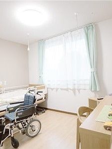 ベッドサイドには緊急通報装置が付いた居室には寝具付きのベッドや車いすがあり、デスクセットも置かれている。