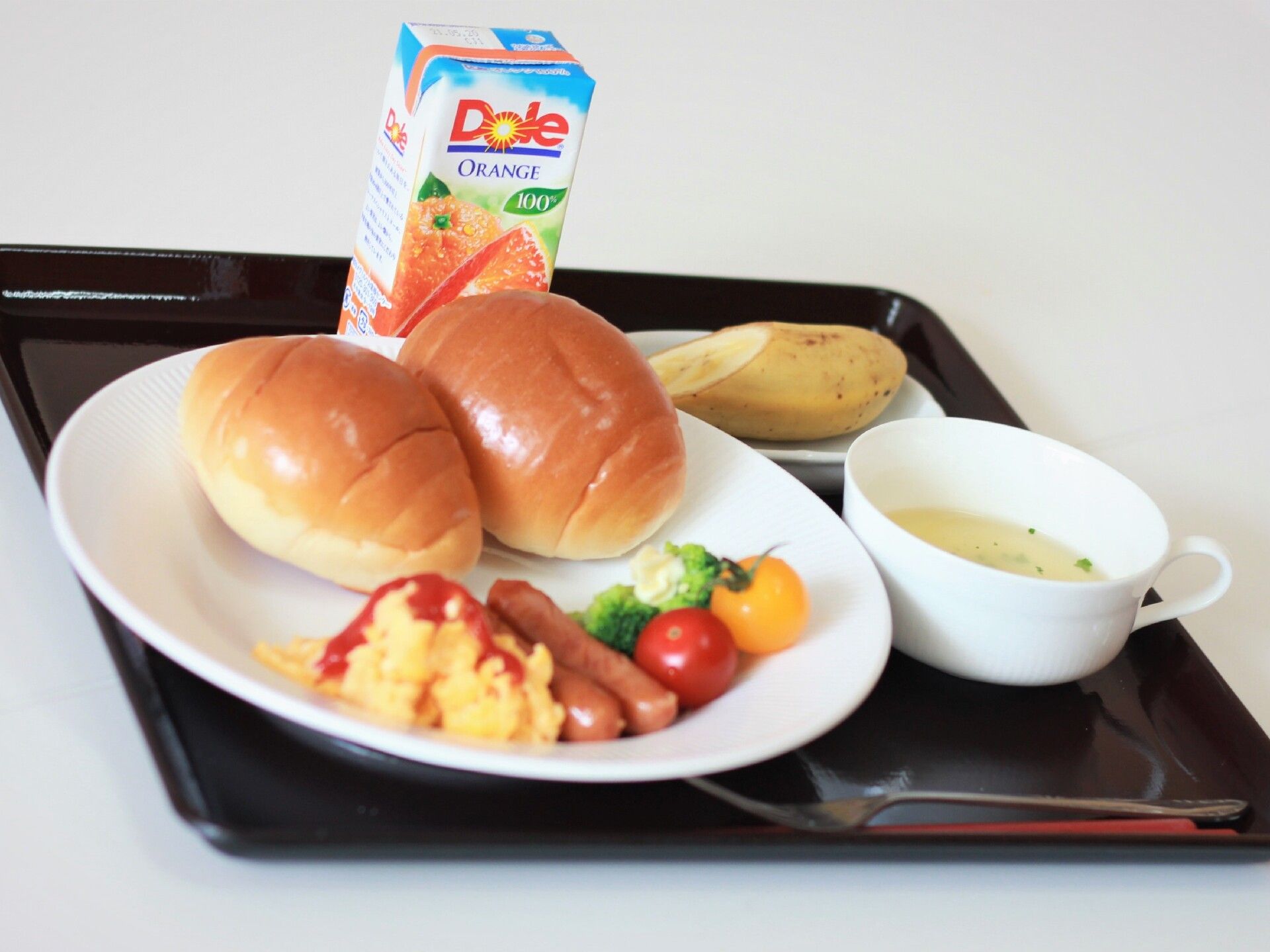 スクランブルエッグとソーセージ、バターロールにスープとバナナ、パックのジュースが付いた食事