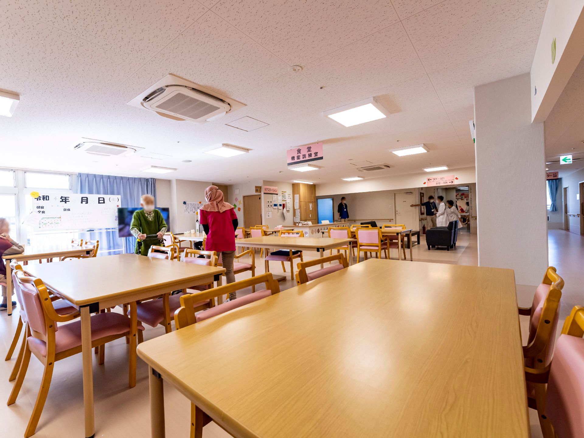 ピンクの介護用の椅子とブラウンのテーブルが設置された共有スペース
