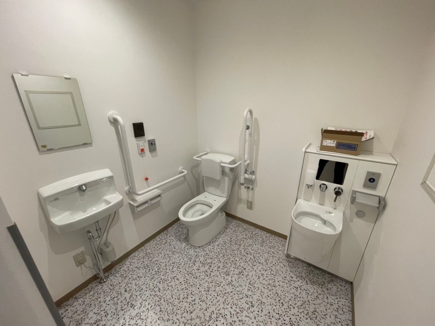 オストメイト対応のトイレは広く、便座には手すりや背もたれが付き、オレンジの呼び出しボタンもある。