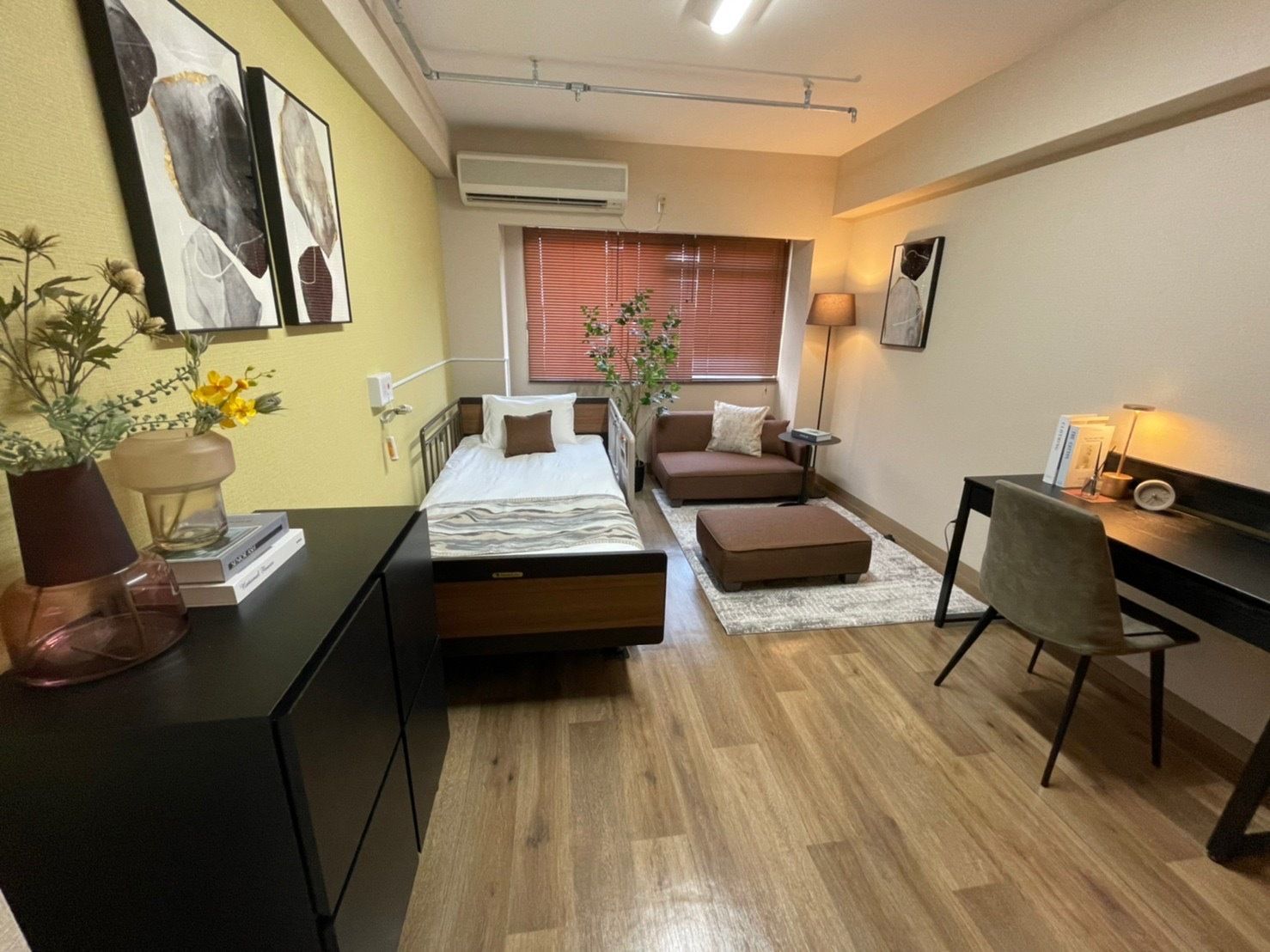 フローリングの部屋には介護ベッドやローソファが置かれ、観葉植物や絵画も飾られている。