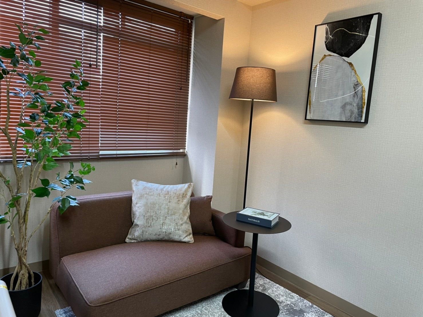 クッションが置かれたブラウンのソファがある部屋には観葉植物が飾られ、絵画も飾られている。