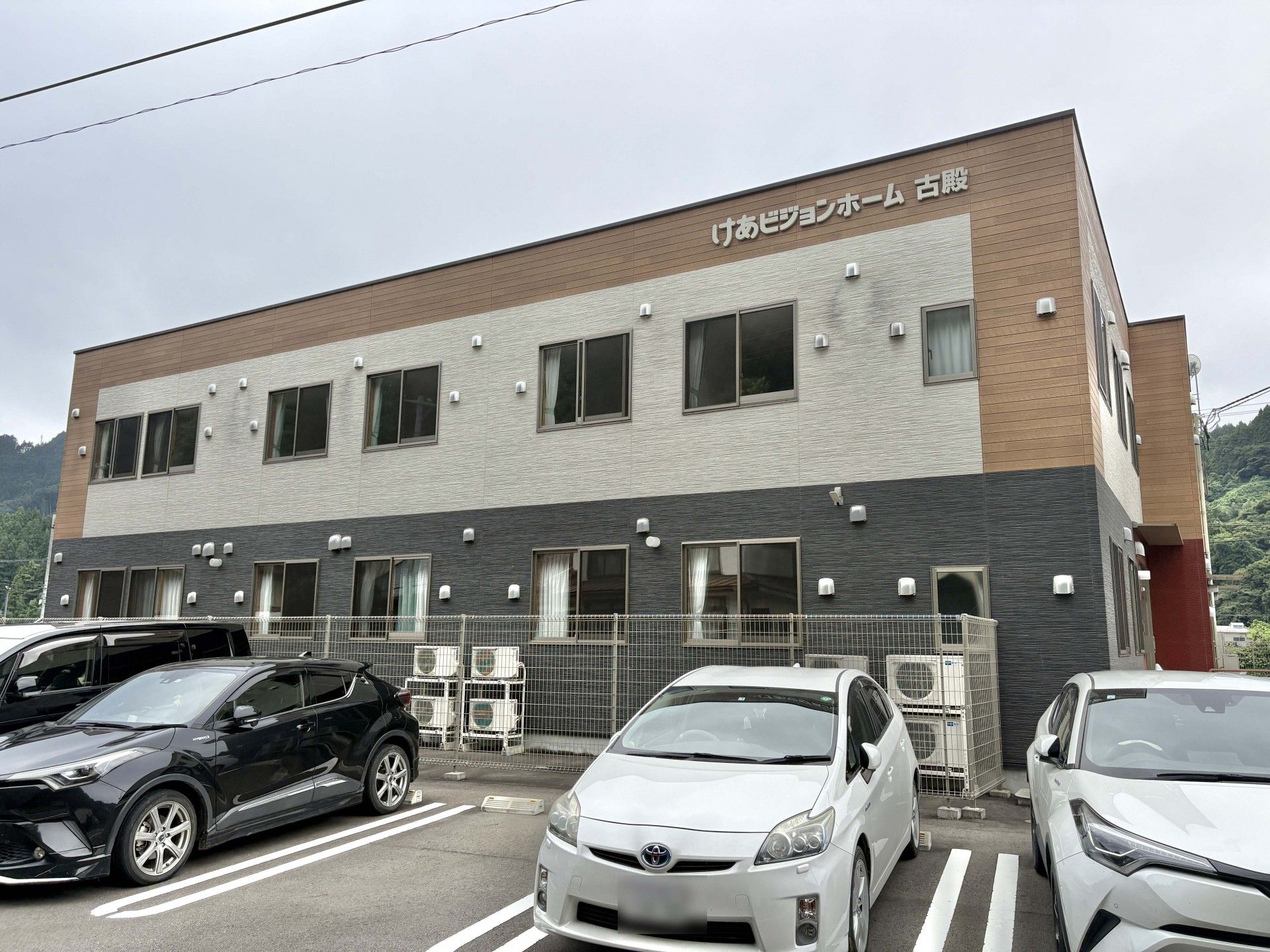 白い服を着た高齢女性のそばには青いユニフォームを着た男性スタッフがいて、一緒に体操をしている。二人とも大きな口を開けて笑っている。