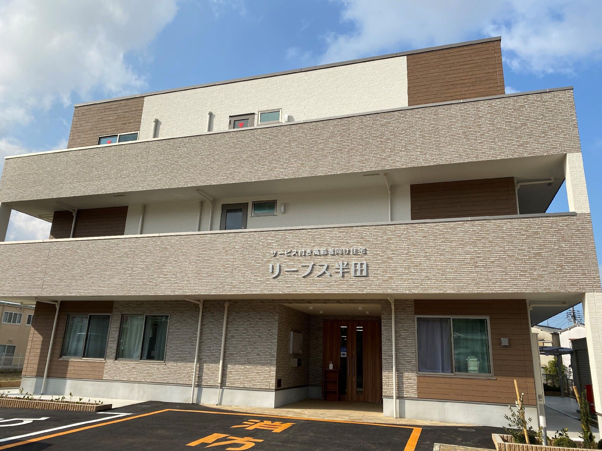 こちらを向いて笑顔になる車いすの高齢女性と介護施設の女性スタッフの様子