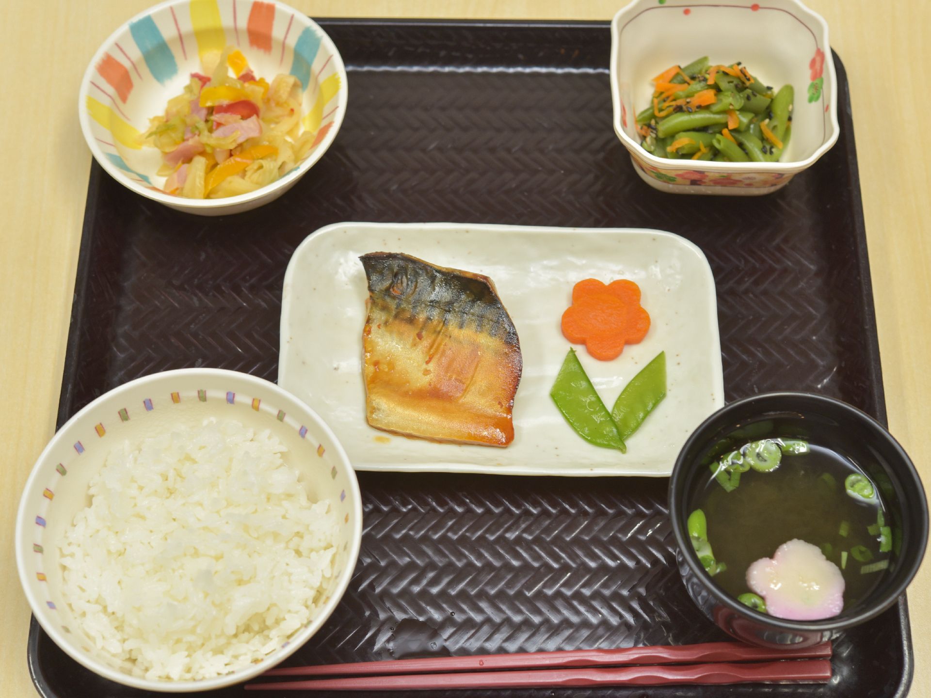 赤い塗り箸がついたお膳がテーブルの上に置いてある。魚の横に飾り切りされた野菜が盛り付けてあり、見た目もきれいである。
