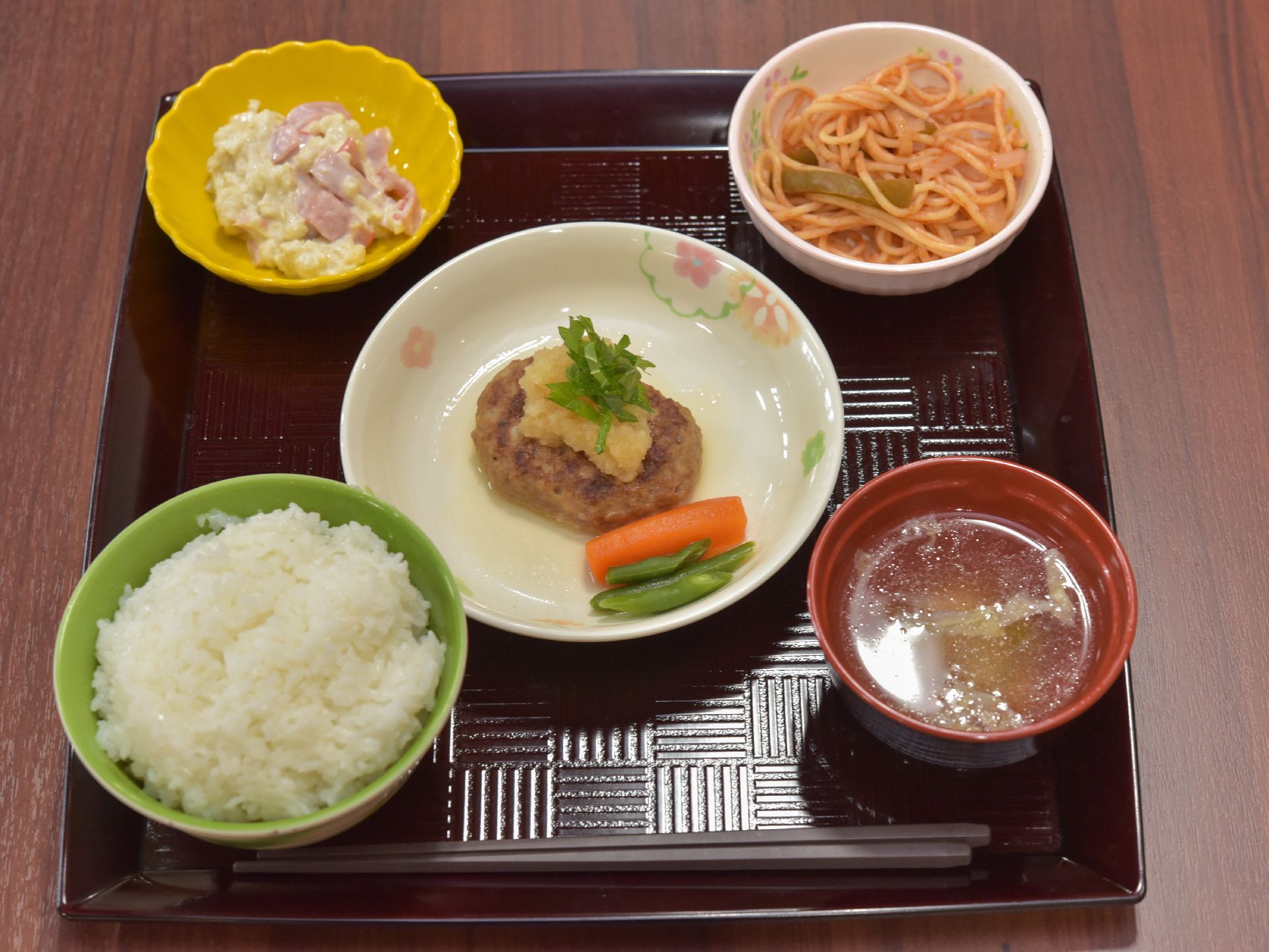 彩の良い食器にごはん、マカロニサラダなどがもっていて、見ためもよく盛り付けてある。メインのおかずはハンバーグで、おろしがそえてある。