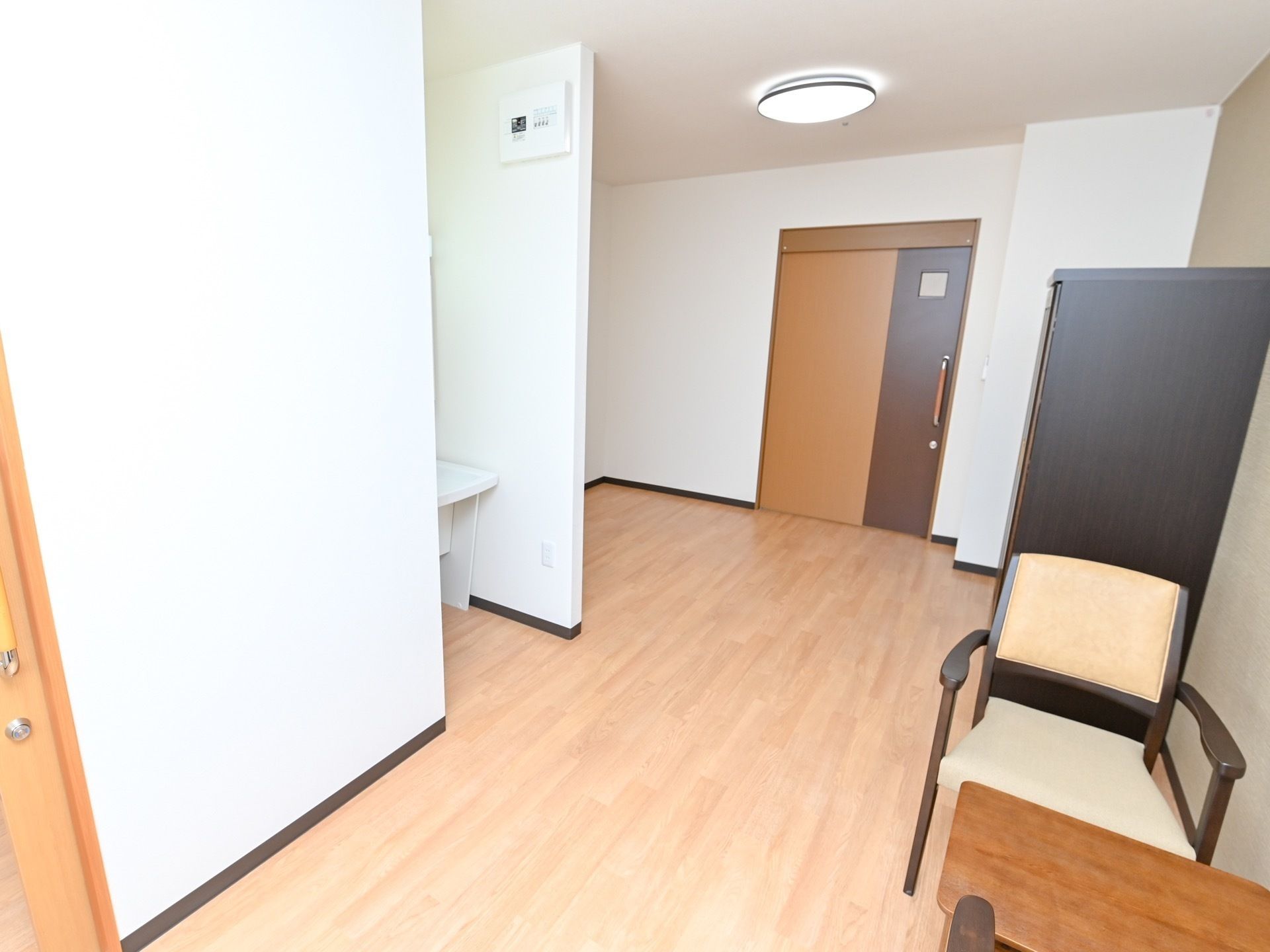白とブラウンで統一された居室である。部屋には、テーブルや椅子が置かれており、入口の扉はスライドドアを採用している。