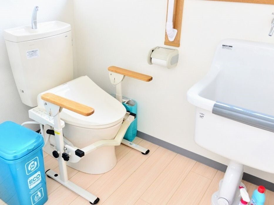 便座の両サイドに手すりが付いたトイレは広く、手洗いができる場所やゴミ箱もあり、壁にも手すりが設置されている。