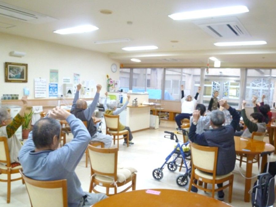 椅子に座ったまま運動している高齢者とそれを指導するスタッフの様子