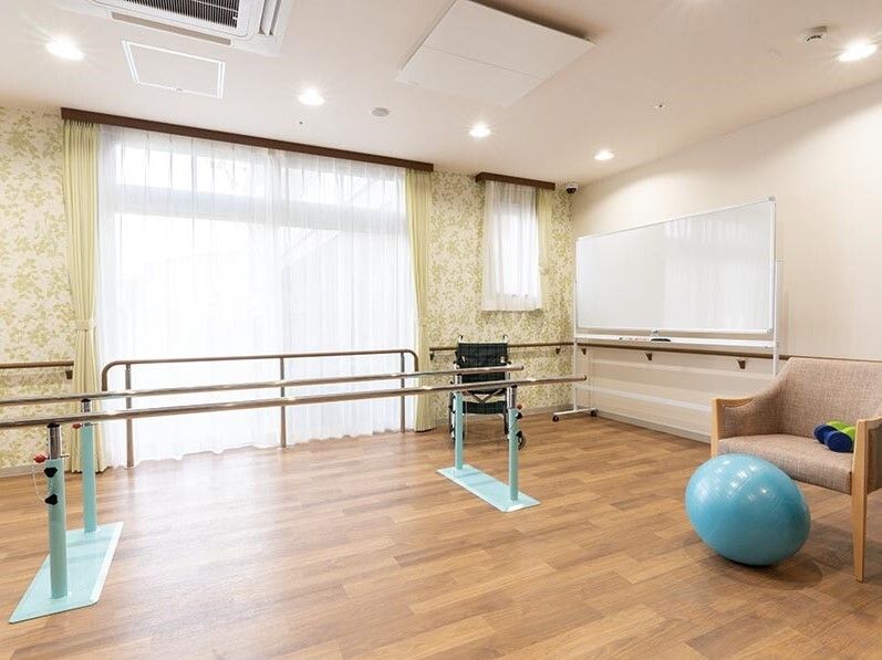 青いボールが椅子の前に置かれ、部屋の中央には平行棒が設置され、大きな窓にはカーテンが付いている。