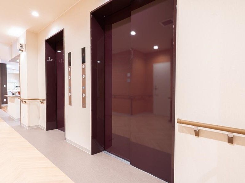 エンジがかったブラウンのドアが付いたワイドタイプのエレベーターが2基設置された館内。壁には手すりが付いている。