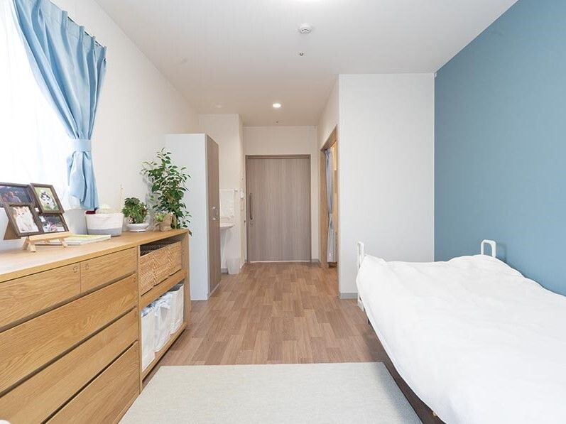 白とライトブルーでまとめられた部屋には寝具がセットされたベッドや木製のタンスなどがあり、観葉植物が飾られている。