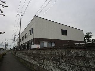 2階建ての建物はフロアにより外壁の色が異なり、建物の周囲にはブロック塀が建てられている。