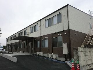 2階建ての建物はフロアにより外壁の色が異なり、敷地内には駐車場があり、側面には屋外階段が設置されている。