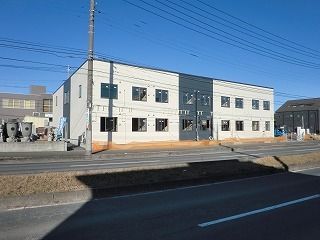 2階建ての建物は横に長く、両サイドが白、中央がダークグレーの外壁。敷地内には駐車場もある。