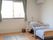 エアコンが付いたフローリングの部屋にはグリーンのカーテンが付いた大きな窓があり、寝具付きのベッドのそばには緊急通報装置がある。