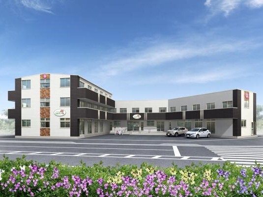 コの字型の３階建て、一部２階建ての建物。白とダークグレーでまとめられ、道路に面している。