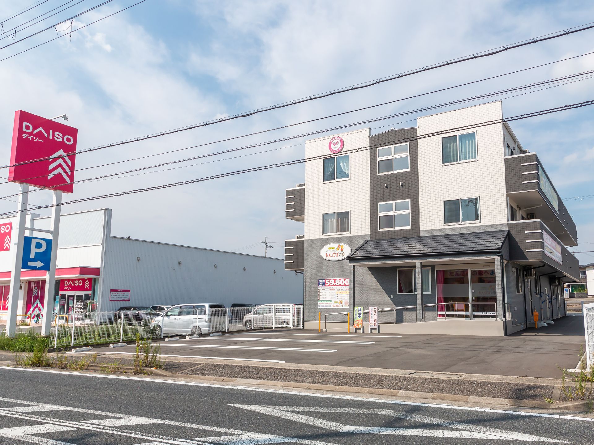 駐車場に隣接した白と黒の外観で３階建ての建物