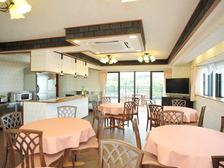 4人用の円形のテーブルセットが複数置かれた食堂。それぞれのテーブルにはサーモンピンクのテーブルクロスがかけられている。