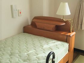 マットレス付きの木製のベッドが置かれていて、ライトも付いている。ベッドサイドには緊急通報装置があり、寝たまま押すことができる。
