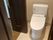 大理石のようなフロアにシンプルなデザインのトイレが設置され、壁にはトイレットペーパーホルダーと操作パネルが付いている。
