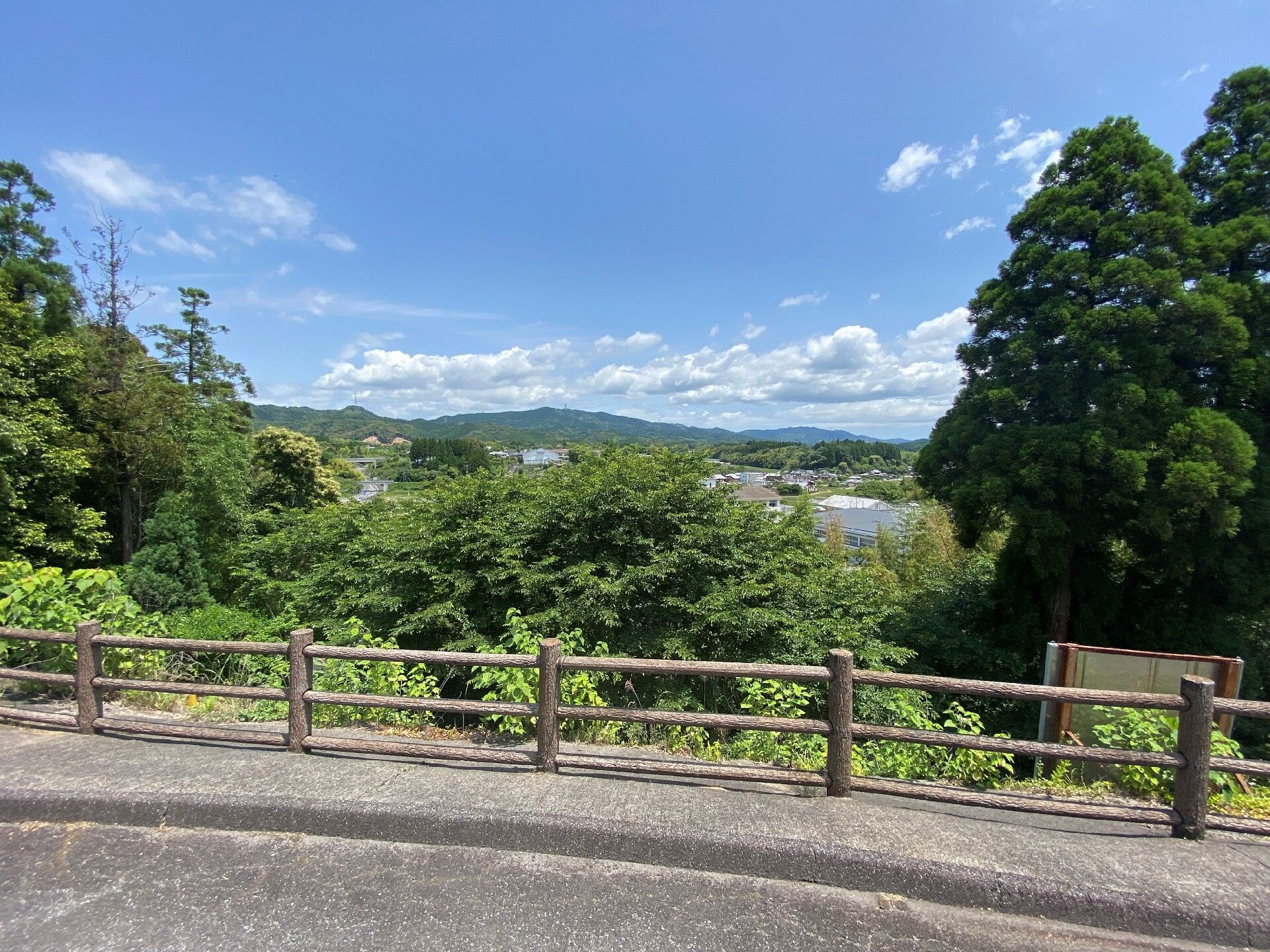 遠くには青い山々が連なっていて、手前には街並みが広がっている。空には白い雲が点在している。