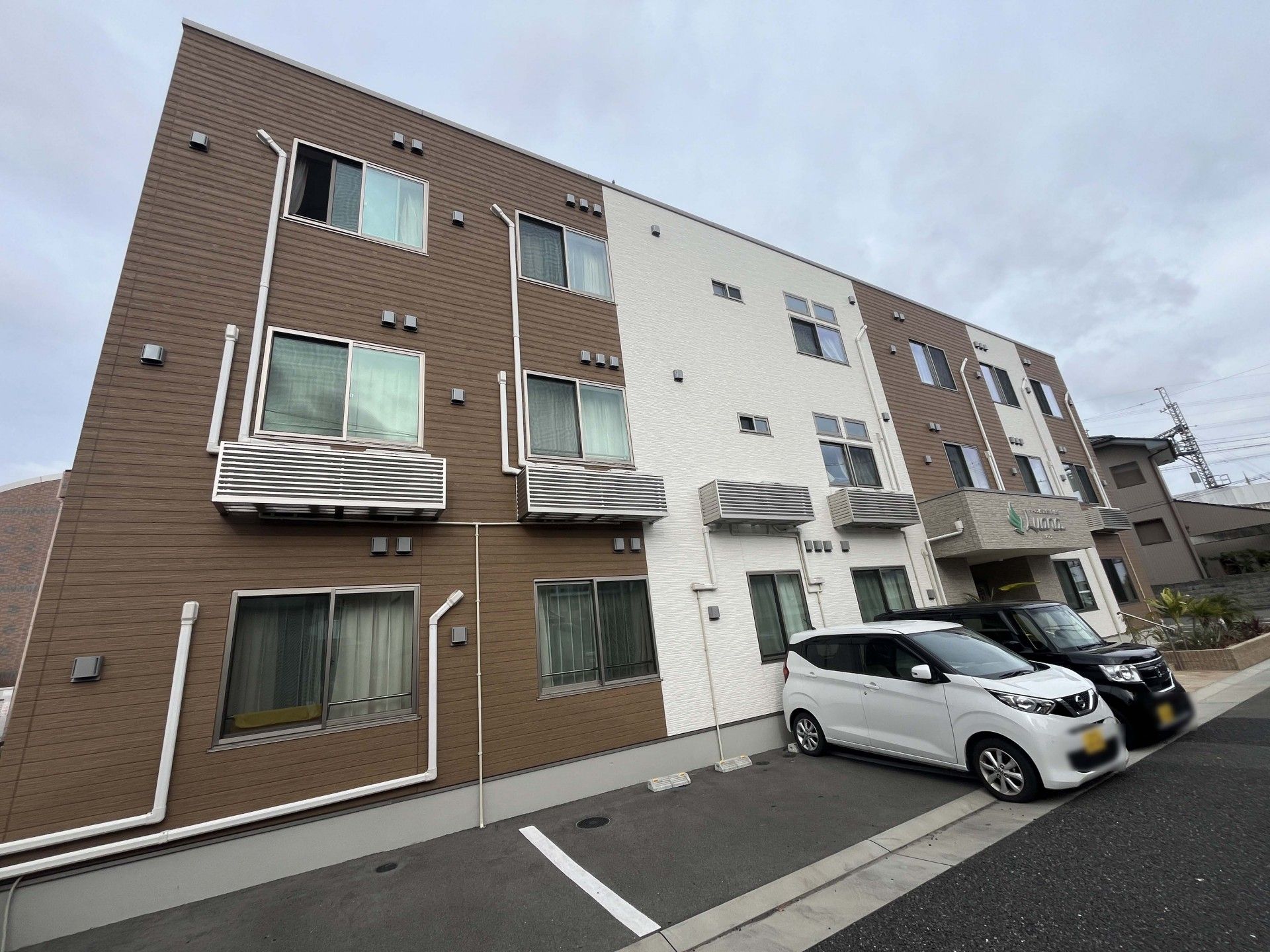 ブルーのエプロンを付けた女性スタッフに付き添われて屋外で過ごしているニット帽をかぶった高齢女性。女性は車いすに座っている。