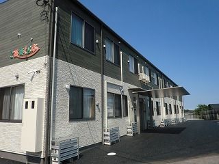 1階部分が白、2階部分がダークグレーの2階建ての建物は玄関に車寄せがあり、敷地内には駐車場がある。