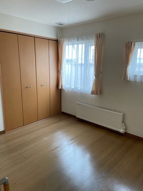 大きな収納スペースが付いたフローリングの部屋には大きな窓があり、カーテンが付いている。窓の下にはパネルヒーターがある。