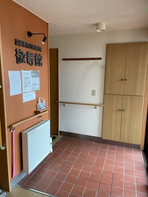 レンガ色のタイルが敷かれた玄関の壁には木目調の手すりが付き、扉付きの靴箱もあり、掲示板には張り紙がされている。