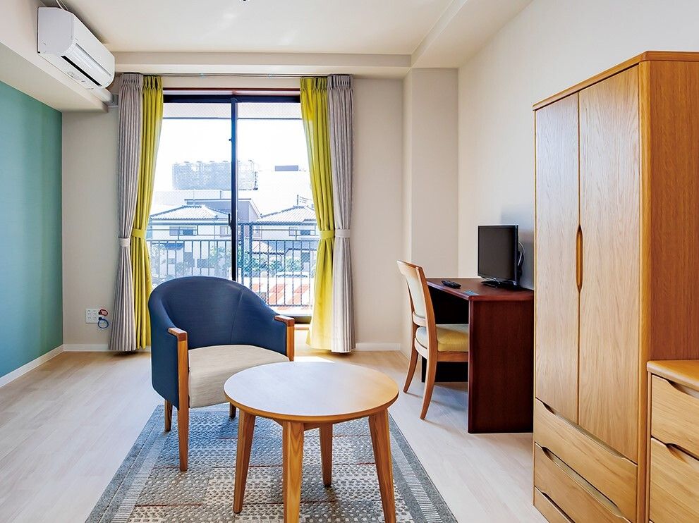 エアコン付きの部屋にはテーブルセットや大小の収納家具があり、大きな窓が付いている。