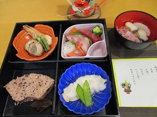 扇側の赤飯やエビなどの煮物、刺身の盛り合わせ、かぶら蒸しが4つに区切られた弁当風の箱に詰められ、にゅう麺が入った汁が添えられている。
