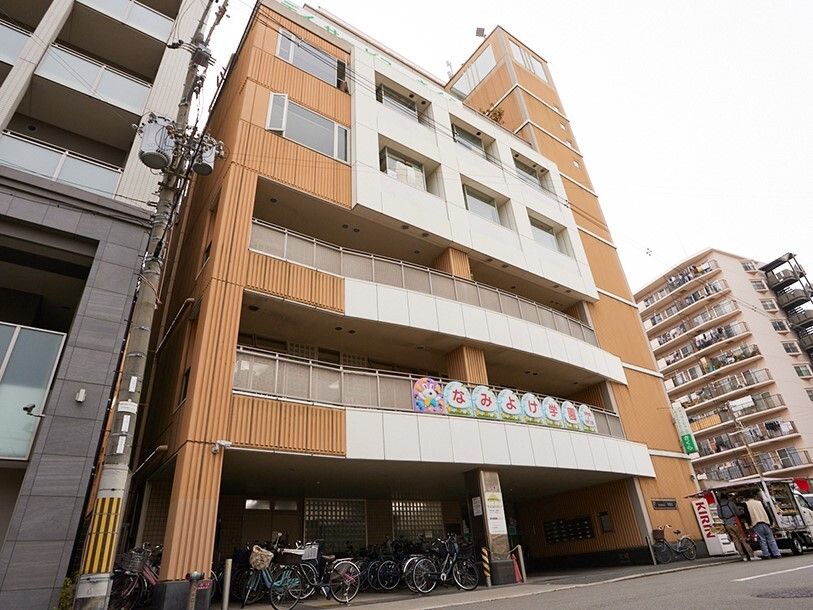 白とブラウンの建物は1階部分に駐輪場があり、2階と3階にはベランダが付き、周りにもたくさんのビルがある。