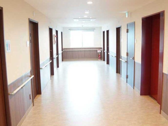 左にはトイレのマークが貼られた場所があり、右側にはエレベーターがあり、まっすぐな廊下は全域壁に手すりが付いている。