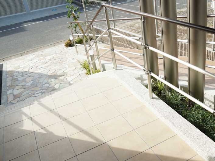 道路に面した建物のエントランス周辺。階段とスロープの両方が設置されていて、手すりも付いている。建物の周りにはフェンスもある。