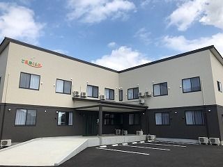 エル字型の2階建ての建物は玄関からスロープが伸びていて、各フロアの外壁の色が異なる。
