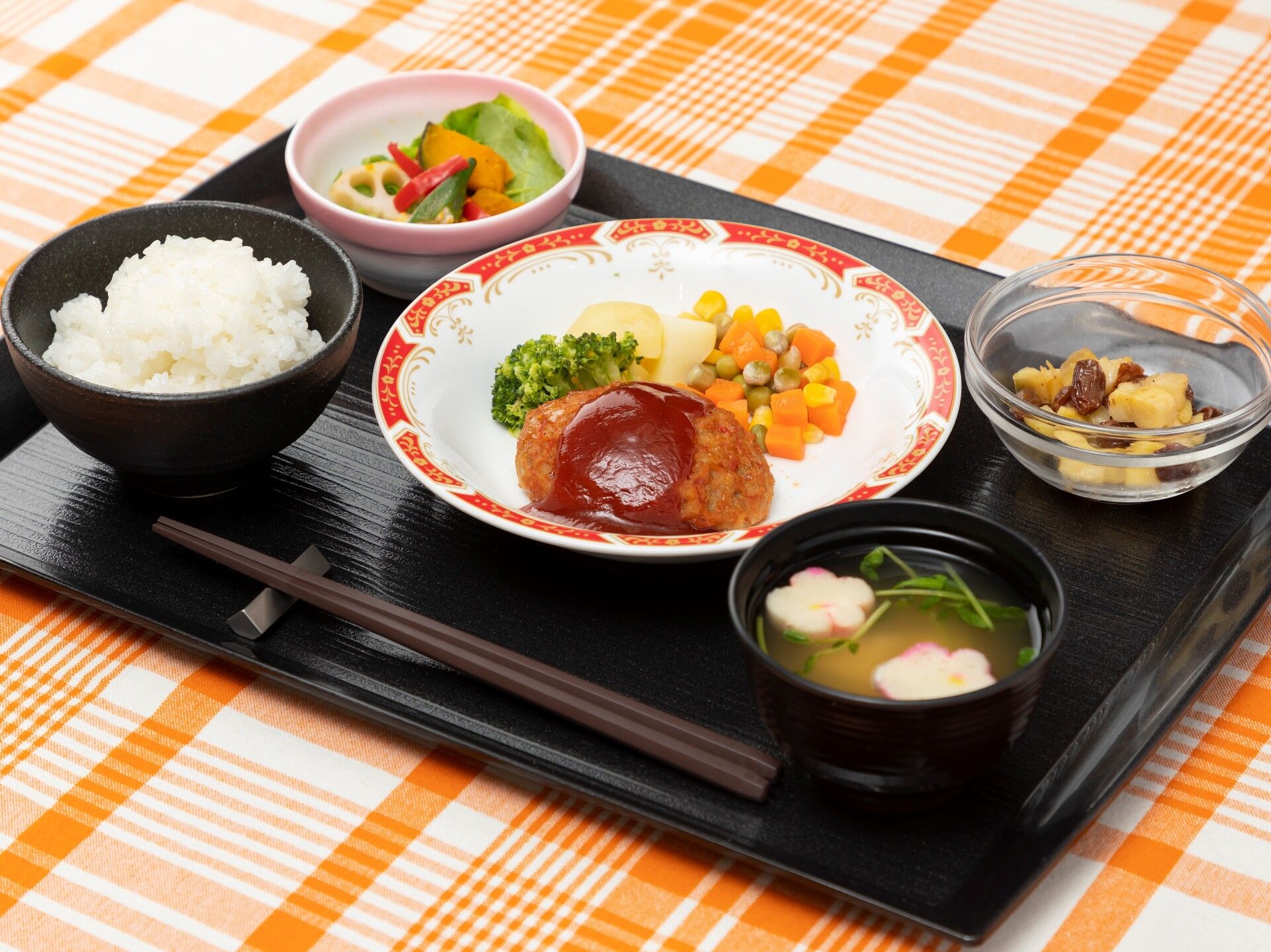 白いご飯に味噌汁、ソースがかかったハンバーグには温野菜が添えられ、サラダや野菜の和え物もある。