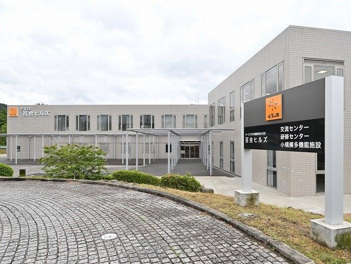 2階建ての建物はエル字型で、外壁にはオレンジのシンボルマークと住宅名があり、ロータリーも付いている。