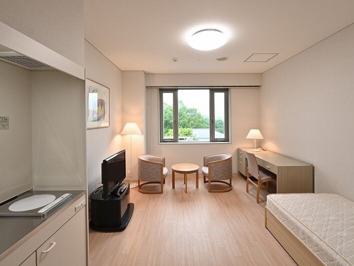 まっすぐな廊下の両サイドに手すりと居室のドアがあり、右側に行く通路もある。突き当りには大きな窓が付いている。