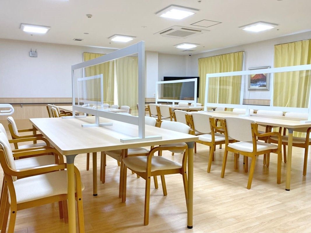 木製のダイニングテーブルセットが複数置かれている食堂。テーブルにはアクリル板も設置されている。